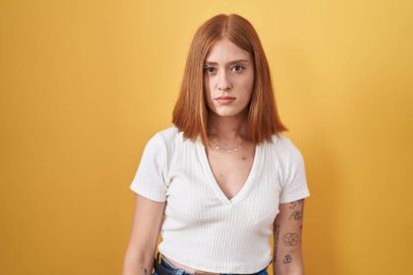 Sarı arka planda duran genç kızıl saçlı kadın şüpheci ve gergin, sorun yüzünden surat asıyor. negatif kişi. 