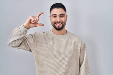İzole edilmiş arka planda duran yakışıklı genç adam gülümsüyor ve el hareketleriyle hareket ediyor parmaklarıyla işaret yapıyor ve kameraya bakıyor. Ölçü kavramı. 