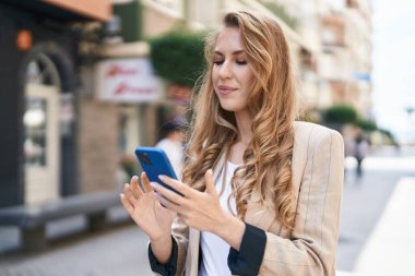 Sokakta akıllı telefon kullanan, kendine güvenen genç sarışın kadın.