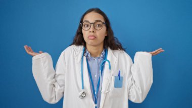 Genç, güzel İspanyol kadın doktor, soyutlanmış mavi arka planda bilgisiz duruyor.