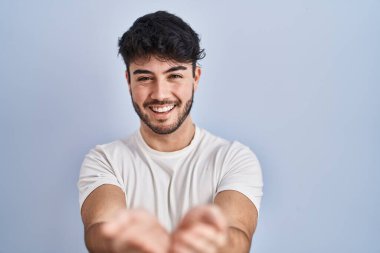 Hispanic man with beard standing over white background smiling with hands palms together receiving or giving gesture. hold and protection 