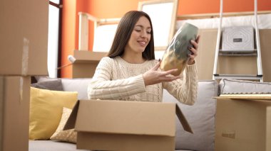 Genç, güzel, İspanyol bir kadın gülerek yeni evindeki karton kutuları açıyor.