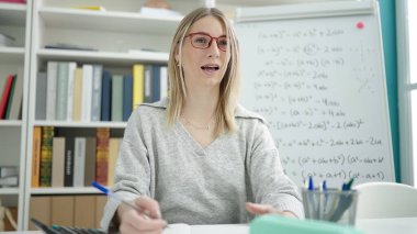 Kütüphane üniversitesinde masa başında matematik dersi veren genç sarışın kadın.