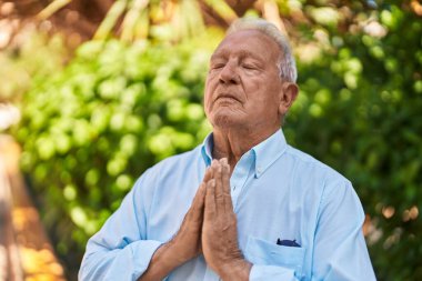 Yaşlı gri saçlı adam parkta dua ediyor.