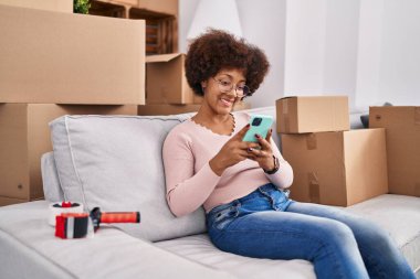 Evdeki koltukta oturan Afro-Amerikan kadın akıllı telefon kullanıyor