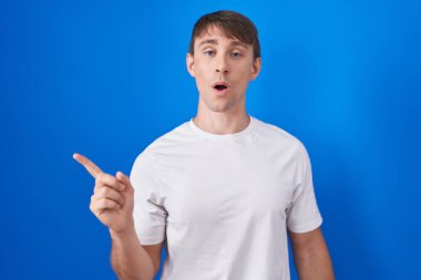 Mavi arka planda dikilen beyaz, sarışın adam şaşırdı. Parmağını yana kaldırdı, ağzı açık hayret içinde kaldı.. 