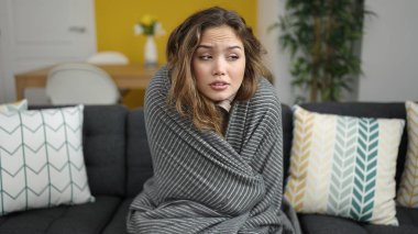 Young beautiful hispanic woman covering with blanket for cold at home