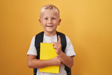 Küçük beyaz çocuk öğrenci çantası takıyor ve elinde bir fikirle ya da soru sorarak şaşırmış bir numara, mutlu yüzle işaret ediyor. 