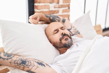 Genç kel adam yatak odasında kollarını esneterek uyanıyor.