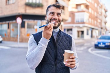 Genç İspanyol adam akıllı telefonda konuşuyor. Sokakta kahve içiyor.