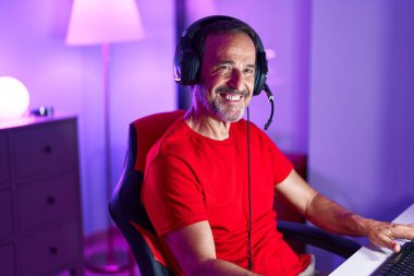 Oyun masasında oturan orta yaşlı adam gülümsüyor.