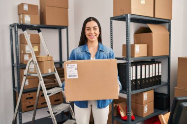 Küçük işletme şirketinde çalışan İspanyol bir kadın, elinde tuttuğu kutuda mutlu ve havalı bir gülümsemeyle gülümsüyor. diş gösterme. 