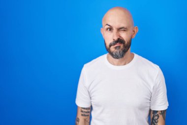 Mavi arka planda duran İspanyol dövmeli adam kameraya seksi bir ifadeyle bakıyor, neşeli ve mutlu bir yüzle.. 