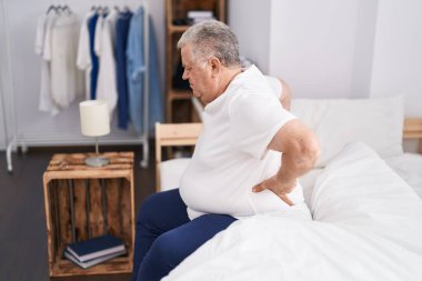 Middle age grey-haired man suffering for back injury sitting on bed at bedroom
