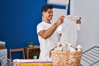 Genç İspanyol adam gülümsüyor. Çamaşır odasında kendine güveni tam bir elbise asıyor.