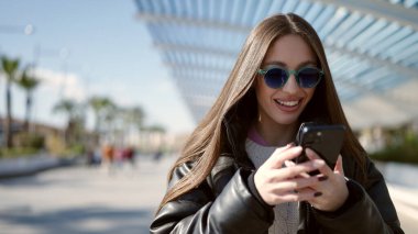 Parkta akıllı telefon kullanarak gülümseyen güzel bir İspanyol kadın.