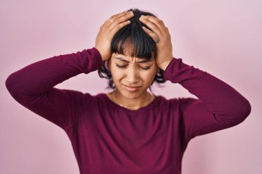 Pembe arka planda duran genç ve güzel bir kadın. Baş ağrısı, çaresiz ve stresli. Çünkü acı ve migren. Eller başının üstünde.. 