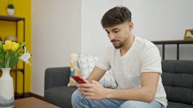 Young arab man using smartphone sitting on sofa at home