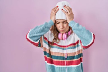 Young blonde woman standing over pink background suffering from headache desperate and stressed because pain and migraine. hands on head. 