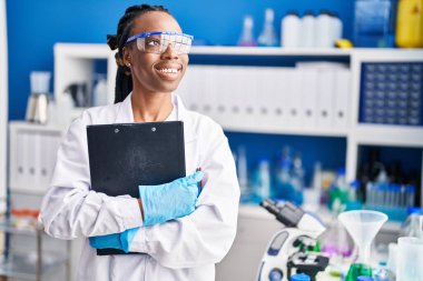 Afrikalı Amerikalı bilim kadını gülümsüyor. Laboratuvarda elinde bir pano var.