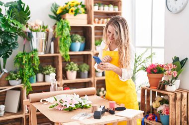 Young blonde woman florist make photo to flowers by smartphone at florist