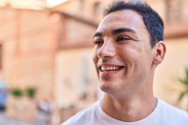 Young hispanic man smiling confident looking to the side at street