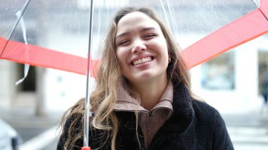 Young beautiful hispanic woman smiling confident holding umbrella at street