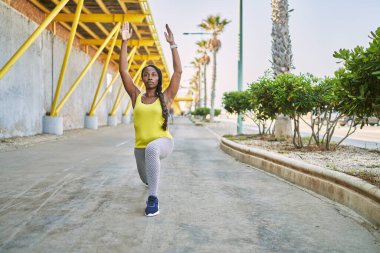 Spor kıyafetleri giyen Afrikalı Amerikalı kadın sokakta yoga egzersizi yapıyor.