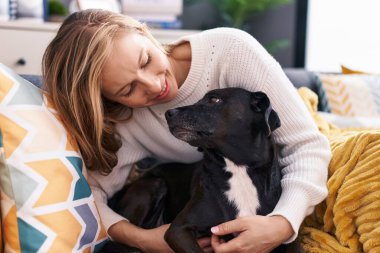 Young blonde woman hugging dog sitting on sofa at home