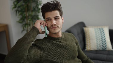 Genç İspanyol adam evde rahat bir ifadeyle akıllı telefondan konuşuyor.