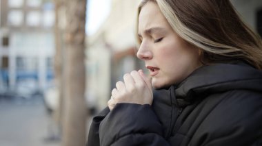 Young blonde woman praying with closed eyes at street