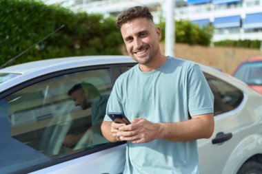 Young hispanic man using smartphone leaning on car at street