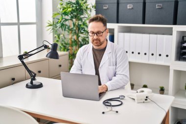 Klinikte çalışan genç beyaz bir doktor dizüstü bilgisayar kullanıyor.