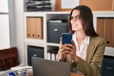 Ofiste çalışan genç ve güzel İspanyol iş kadını akıllı telefon kullanıyor.