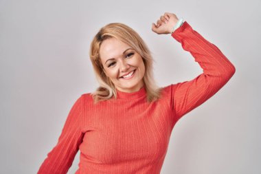 Sarışın kadın arka planda durmuş dans ediyor mutlu ve neşeli, gülümsüyor hareketli ve kendinden emin müzik dinliyor. 