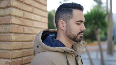 Latin kökenli genç adam ciddi bir ifadeyle sokağa bakıyor.