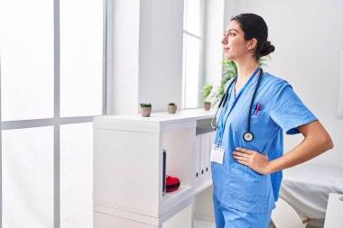 Young beautiful hispanic woman doctor looking through the window at clinic