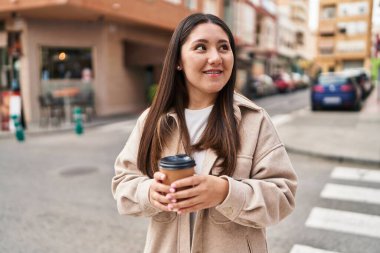 Young hispanic woman smiling confident drinking coffee at street