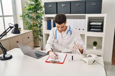 Doktor üniforması giyen İspanyol genç adam klinikte kan testi tüpünü inceliyor.