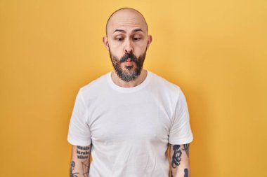 Sarı arka planda duran İspanyol dövmeli genç adam dudaklarıyla balık suratı yapıyor, çılgınca ve komik bir jest. Komik ifade. 