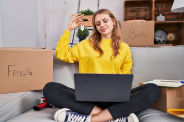 Young blonde woman having video call holding key at new home