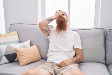 Young redhead man stressed sitting on sofa at home