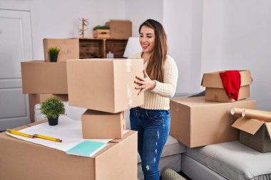Young beautiful hispanic woman smiling confident holding package at new home