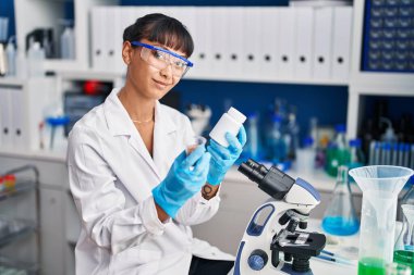 Genç ve güzel İspanyol bilim adamı gülümsüyor. Laboratuvarda ilaç şişesi tutuyor.