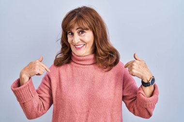 Orta yaşlı İspanyol bir kadın izole bir arka planda duruyor. Yüzünde bir gülümsemeyle, gururlu ve mutlu bir şekilde kendini işaret ediyor.. 