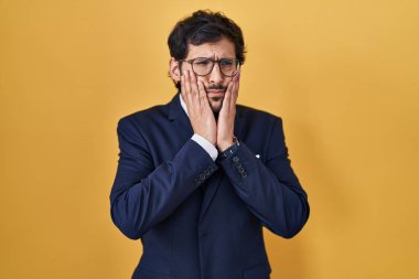 Sarı arka planda duran yakışıklı Latin adam yorgun eller yüzünü, depresyonu ve üzüntüyü örten, sorun yüzünden üzgün ve sinirli. 