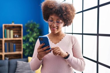 Afro-Amerikalı kadın evde akıllı telefon kullanarak gülümsüyor.