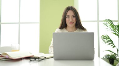 Young beautiful hispanic woman student smiling confident using laptop studying at home