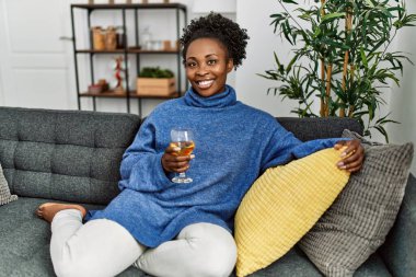 Afro-Amerikalı bir kadın evdeki masada oturmuş şarap içiyor.