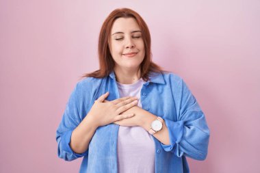 Pembe arka planda duran, elleri göğsünde, gözleri kapalı ve yüzünde minnet dolu bir jestle gülümseyen İspanyol bir kadın. sağlık kavramı. 